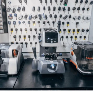 Car key cutting machines on a workbench in a locksmith workshop with key blanks hanging on the wall.