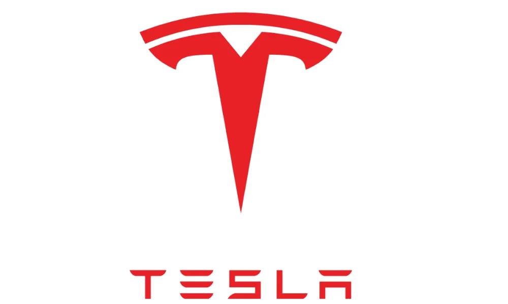 A red Tesla logo displayed prominently against a plain white background. The image features Tesla’s stylized red “T” emblem near the top, with the pointed vertical stem and curved upper shape forming the recognizable Tesla symbol. The word “TESLA” appears below the emblem in matching red lettering with Tesla’s distinctive stylized typography. The image represents the Tesla automotive brand.
