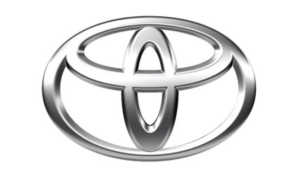 A silver Toyota car logo displayed prominently against a plain white background. The emblem features Toyota’s distinctive oval design with three overlapping oval shapes forming the stylized Toyota symbol, rendered in a metallic silver finish with darker gray shading that gives the logo a dimensional appearance. The image represents the Toyota automotive.