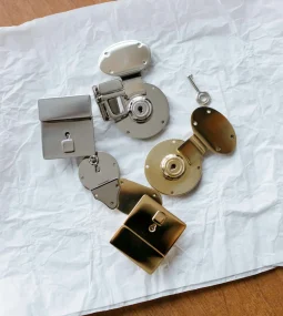 Overhead view of several metal door lock components, including latch mechanisms, square and round lock bodies, and strike plates arranged on a white textured surface.